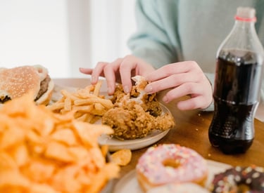 Hands picking apart crispy fried chicken served with french fries, a burger, and donuts.