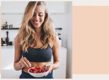 Smiling woman in fitness wear holding a bowl of fresh raspberries and blueberries.