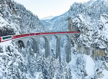 Glacier Express luxury train crossing a snowy viaduct in the Swiss Alps.