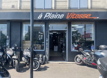 A Plaine Vitesse motorcycle shop storefront with scooters and motorbikes parked outside.