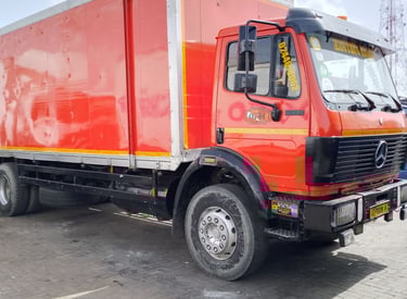 A vibrant red Mercedes-Benz delivery truck with a white enclosed cargo box, yellow and orange accent
