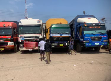 A row of colorful heavy-duty trucks—red MAN, white DAF, yellow flatbed, and blue DAEWOO—parked side 