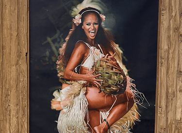 Polynesian hula dancer in traditional grass skirt performing in a rustic wooden frame portrait.