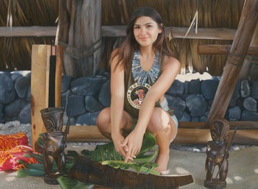 Young woman crouching by traditional Hawaiian tiki carvings and tropical leaves in a tiki hut.