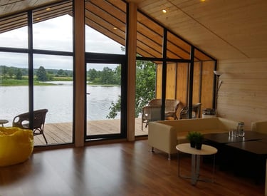 Modern lakeside cabin interior with floor-to-ceiling windows, wood paneling, and a scenic river view.