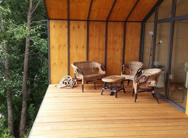 Modern wooden balcony with wicker chairs overlooking a lush green forest.