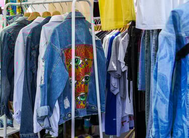 Chamarras de mezclilla y playeras coloridas en perchero en mercado de segunda mano al aire libre