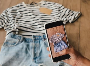 Persona tomando una foto de playera a rayas y shorts de mezclilla con un smartphone para revenderlos