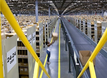 A worker sorting cardboard boxes on a conveyor belt system inside a large distribution warehouse center.