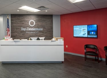 Modern office reception area for Day & Zimmermann with white desk and stone accent wall.