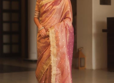 Elegant woman wearing a dusty pink organza silk saree with gold zari embroidery and statement earrings.