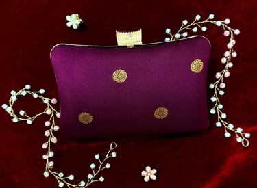 Elegant purple silk clutch bag with gold embroidery on red velvet, featuring floral jewelry accents.