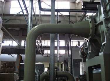 Industrial HVAC ventilation system with large metal pipes and ductwork in a warehouse.