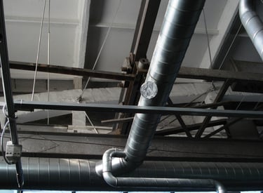 Industrial HVAC spiral ductwork and ventilation pipes installed on a warehouse ceiling.