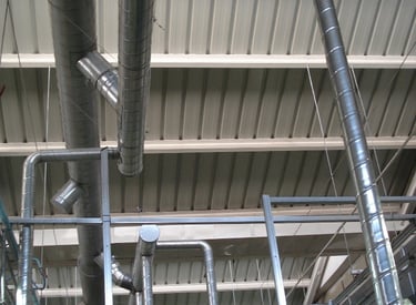 Industrial HVAC spiral ductwork and ventilation pipes installed along a high warehouse ceiling.