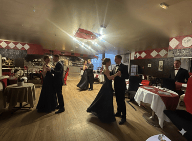 Couples in formal black-tie attire dancing in a ballroom at an elegant gala dinner event.
