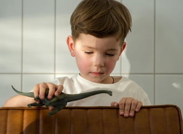 a young boy sitting in a suitcase with a dinosaur toy