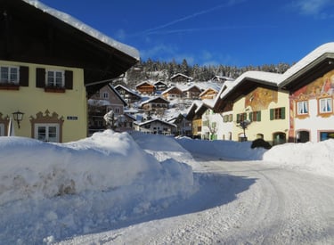 Snow-covered street in a Bavarian village with traditional alpine houses under a clear blue sky.