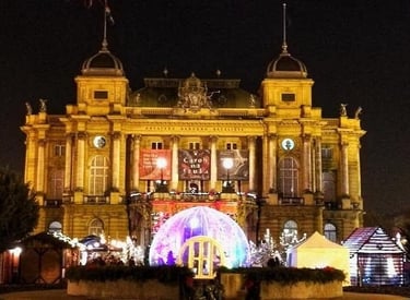 The Croatian National Theatre in Zagreb illuminated at night with festive Christmas market decorations.