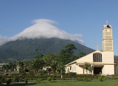 A scenic view of a yellow church with a clock tower and a volcano capped by clouds in Costa Rica.
