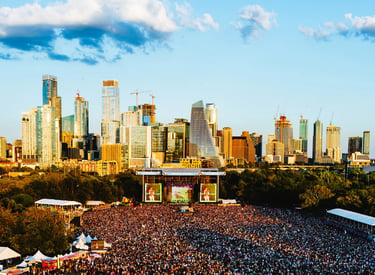 Crowded outdoor music festival at Austin City Limits with the downtown skyline at sunset.