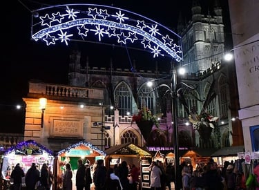 Festive Bath Christmas Market with illuminated star lights in front of Bath Abbey at night.