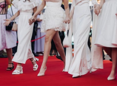 Women in elegant white dresses and high heels walking on a celebrity red carpet event.