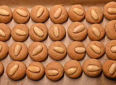 Freshly baked homemade almond cookies topped with whole blanched almonds on a baking sheet.