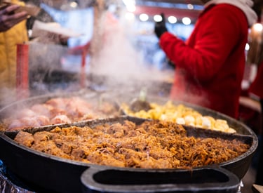 Steaming hot pans of traditional street food including stewed meat and potatoes at a festive European Christmas market.