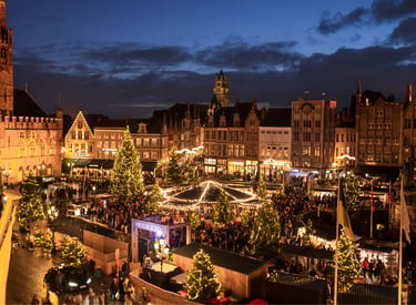 Aerial view of the festive Bruges Christmas market at night with glowing lights and trees.