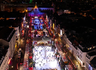 Night aerial view of the Brussels Christmas market with ice skaters and festive lights.