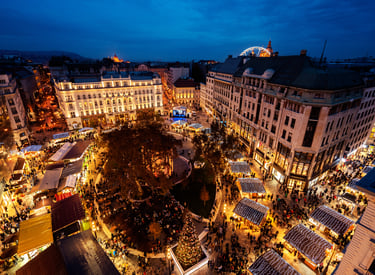 Aerial view of the Budapest Christmas Market at night with festive lights, stalls, and a Ferris wheel.