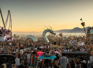 Crowd gathers around a sea serpent art installation and desert art cars at Burning Man festival.