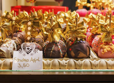 Gourmet chocolate covered apples with gold bows and colorful sprinkles at a European Christmas market stall.
