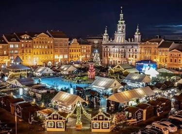 Aerial view of a festive European Christmas market with lit stalls and an ice rink at night.