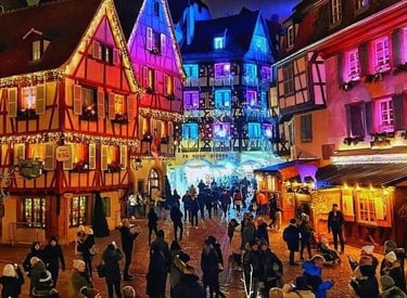 Crowds walking through a festive European Christmas market with colorful illuminated half-timbered houses.