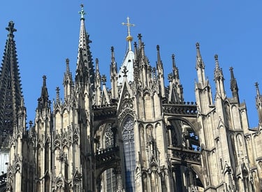 Intricate Gothic architecture and stone spires of the Cologne Cathedral under a clear blue sky.
