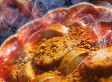 Close-up of steaming hot German currywurst sliced sausage topped with spicy tomato sauce and yellow curry powder.
