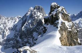 Snow-covered jagged mountain peaks and rocky alpine ridges under a clear blue winter sky.