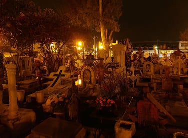 Night view of a Mexican cemetery during Day of the Dead with lit gravestones and flowers.