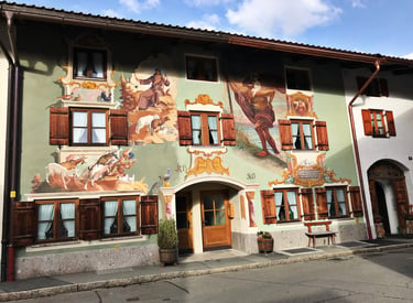 Traditional Bavarian house in Oberammergau featuring ornate religious Lüftlmalerei frescoes and wooden shutters.