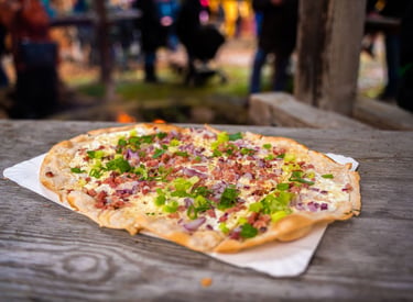 Traditional German Flammkuchen with bacon, onions, and scallions on a rustic wooden table.