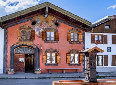 Traditional Bavarian house in Oberammergau with Lüftlmalerei frescoes and a wooden fountain.