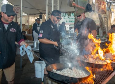 Professional chefs cooking seafood over an open flame grill at a busy outdoor food festival.