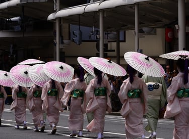 Geisha in pink kimonos walking with traditional floral parasols during a Japanese street parade.