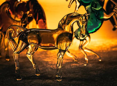 Elegant amber-colored hand-blown glass horse figurine standing on a dark surface with a glowing background.