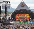 Crowd of people at the Glastonbury Festival Pyramid Stage with peace sign and colorful lights.