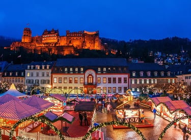 Illuminated Heidelberg Christmas market stalls at night with the historic Heidelberg Castle in the background.