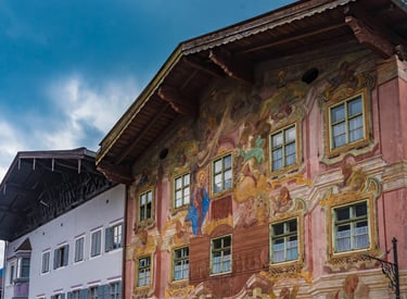 Bavarian house with traditional Lüftlmalerei frescoes and religious murals under a blue sky.