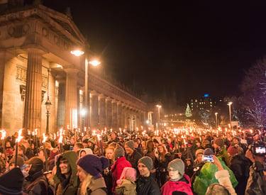 Crowds carry flaming torches past the Royal Scottish Academy during the Edinburgh Hogmanay torchlight procession.